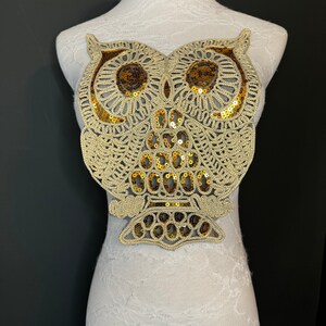 May include: A gold and brown owl applique with sequins. The owl is detailed with a lace-like design.