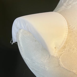 Puede incluir: Tela blanca con una forma curva, posiblemente un cuello o una prenda de vestir. La tela es lisa y tiene un ligero brillo.