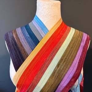 May include: A variety of colorful elastic bands are draped over a mannequin head. The bands are arranged in a rainbow pattern, with shades of blue, purple, red, orange, yellow, green, and brown. The elastic bands are likely used for hair accessories or crafting.