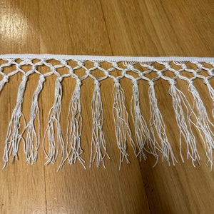 May include: White cotton fringe trim with a knotted design. The fringe is approximately 1 inch long.
