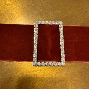 Può includere: Un nastro di velluto rosso con una fibbia argentata decorata con strass trasparenti.