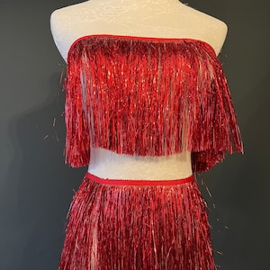 Könnte beinhalten: Ein rotes Oberteil und Rock-Set mit Fransen. Die Fransen bestehen aus glänzendem Metallic-Material.