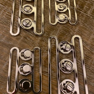 Könnte beinhalten: Vier silberne Gürtelschnallen aus Metall mit jeweils drei runden, dekorativen, silbernen Metallschließen.