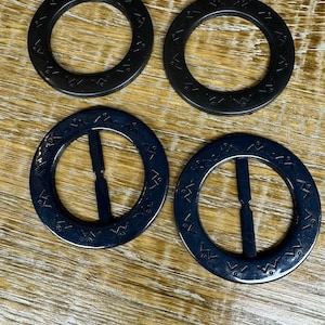 May include: Four black plastic belt buckles with a decorative pattern around the edge. Two of the buckles have a center bar.