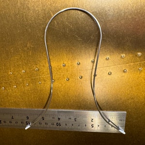 May include: A silver metal headband with white plastic tips on each end. The headband is approximately 15 inches long and is lying on a gold surface.
