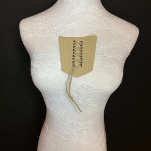 May include: A beige fabric corset-style piece with a lace-up front and brown leather laces. The piece is displayed on a white mannequin.