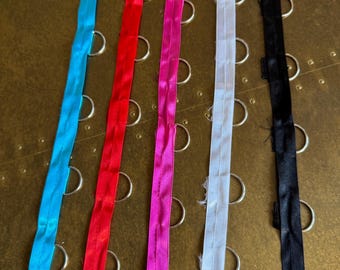 May include: A selection of vibrant zippers in blue, red, pink, white, and black. The zippers are displayed vertically against a textured gold surface, with metal rings visible.