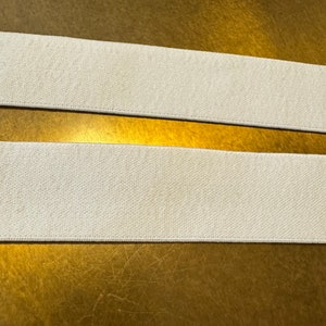Könnte beinhalten: Zwei Stücke weißen elastischen Stoffes, wahrscheinlich für Näh- oder Bastelprojekte.