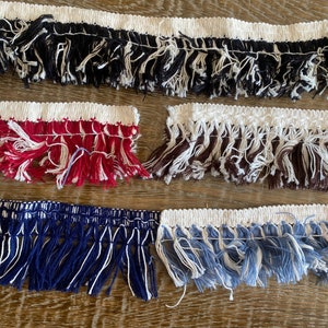 May include: Four different colours of fringe trim with a white backing. The fringe is made of cotton and is available in black, red, brown, and blue.
