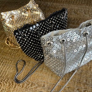 Peut inclure: Trois petits sacs seau avec des bandoulières en chaîne. Les sacs sont recouverts de paillettes et sont disponibles en or, noir et argent.