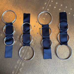 May include: Four silver rings with black ribbon attached. The rings are of different sizes and are arranged in a row.