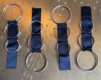 May include: Four silver rings with black ribbon attached. The rings are of different sizes and are arranged in a row.