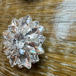 May include: A large, clear crystal embellishment with a faceted design. The crystal is shaped like a flower with multiple points.
