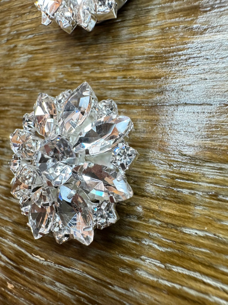 May include: A large, clear crystal embellishment with a faceted design. The crystal is shaped like a flower with multiple points.