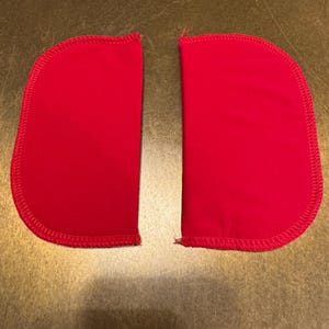 Pode incluir: Dois remendos de tecido vermelho com uma borda arredondada e uma borda costurada.