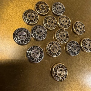 Könnte beinhalten: Eine Sammlung von 14 goldfarbenen Knöpfen mit einem dekorativen Design. Die Knöpfe haben zwei Löcher und eine strukturierte Oberfläche.