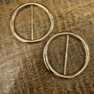 Puede incluir: Dos hebillas de cinturón de metal dorado con un diseño simple y recto.