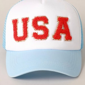 May include: A white and light blue trucker hat with the word "USA" in red letters with gold glitter accents.