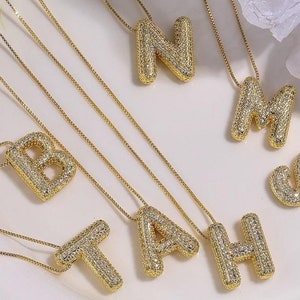 Könnte beinhalten: Ein Satz goldener Halsketten mit Buchstabenanhängern. Jeder Anhänger ist mit kleinen, klaren Strasssteinen besetzt. Die Buchstaben sind B, A, T, H, N, M und S.