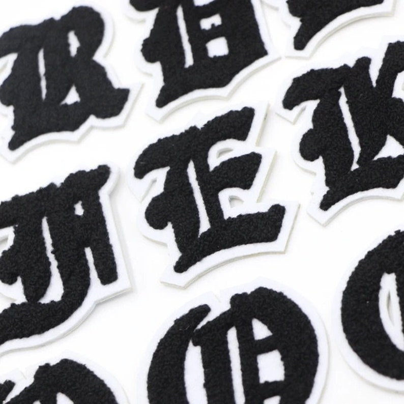 Op de afbeelding: Een set zwarte vilt strijkletters in een oud Engels lettertype. De letters zijn op een witte achtergrond.