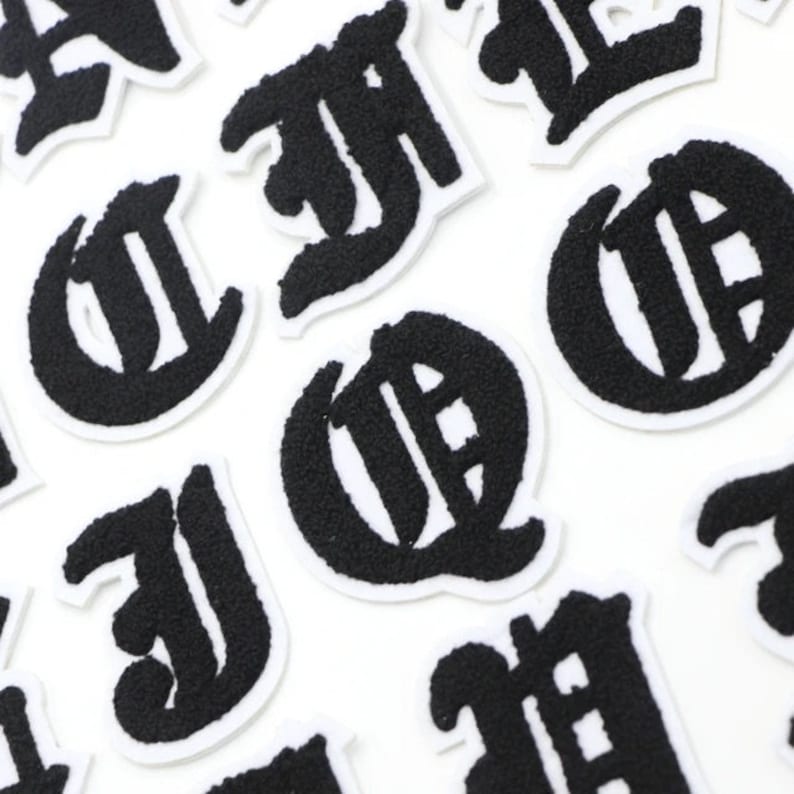 Op de afbeelding: Een set zwarte vilt strijkpatches in de vorm van oude Engelse letters. De letters zijn op een witte achtergrond.