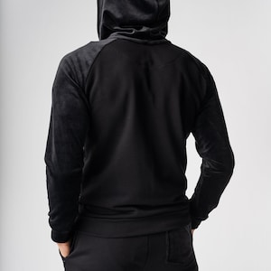 May include: A black hooded sweatshirt with a zipper closure and a matching pair of black sweatpants.
