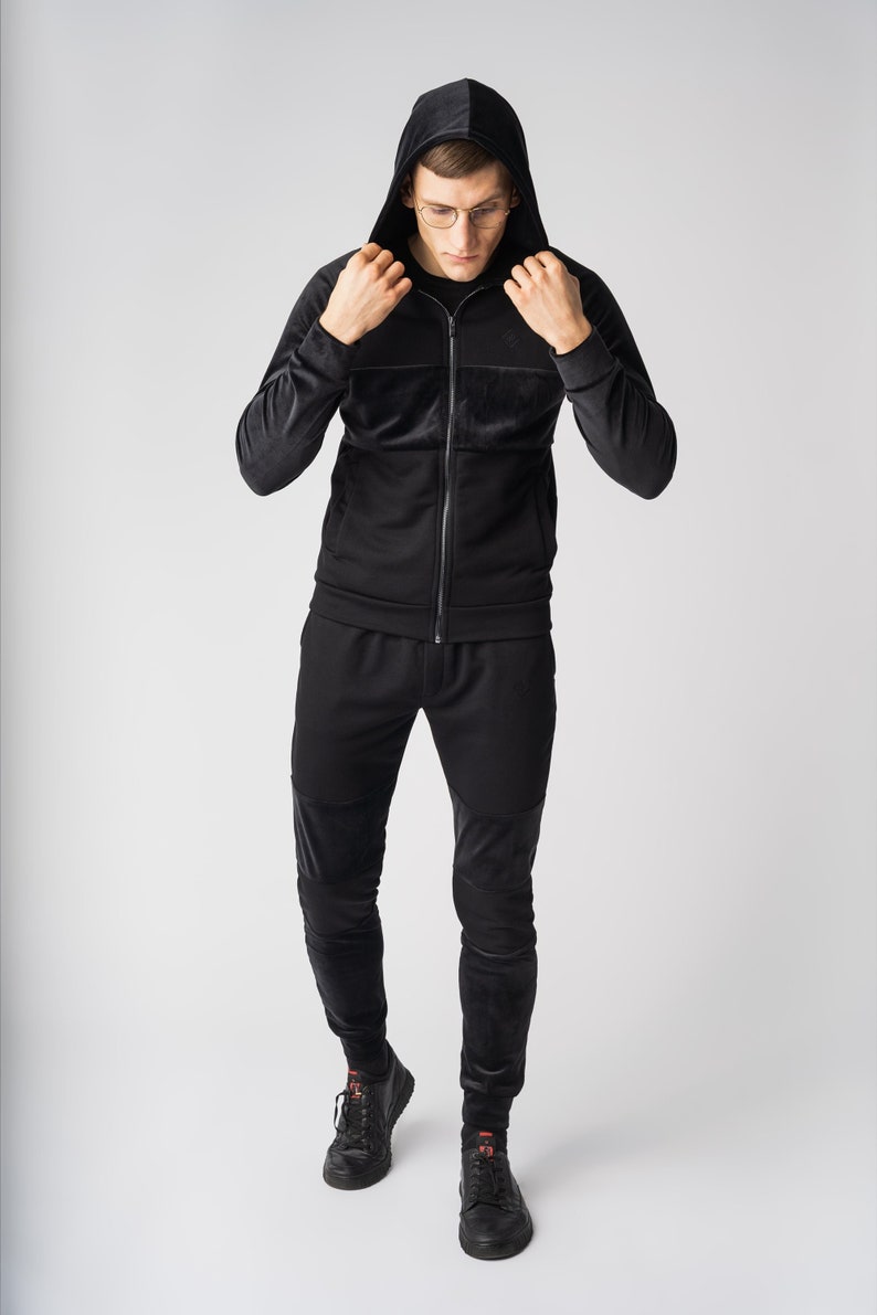 May include: A black hooded sweatshirt and matching sweatpants with a zipper closure. The sweatshirt has a textured design on the chest and sleeves.