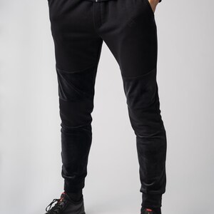 May include: Black sweatpants with velvet panels on the knees and legs. The sweatpants have a drawstring waistband and a small logo on the left leg.