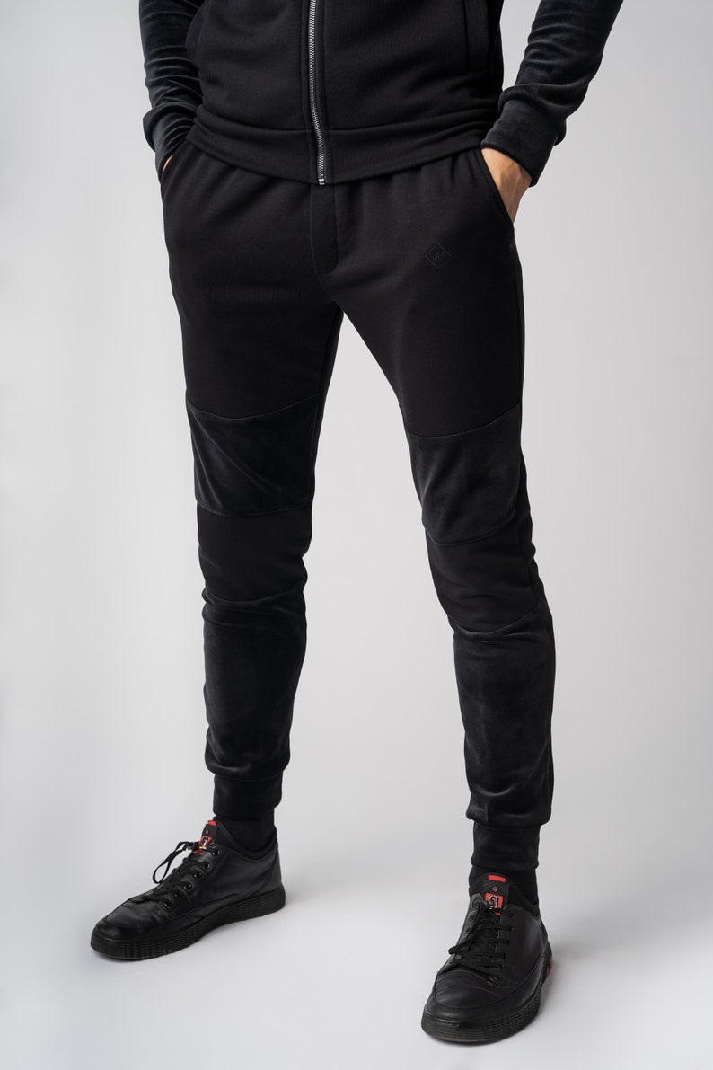May include: Black sweatpants with velvet panels on the knees and legs. The sweatpants have a drawstring waistband and a small logo on the left leg.