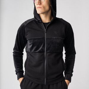 May include: A black zip-up hoodie with a velvet panel and a small diamond logo on the chest. The hoodie has a drawstring hood and long sleeves.