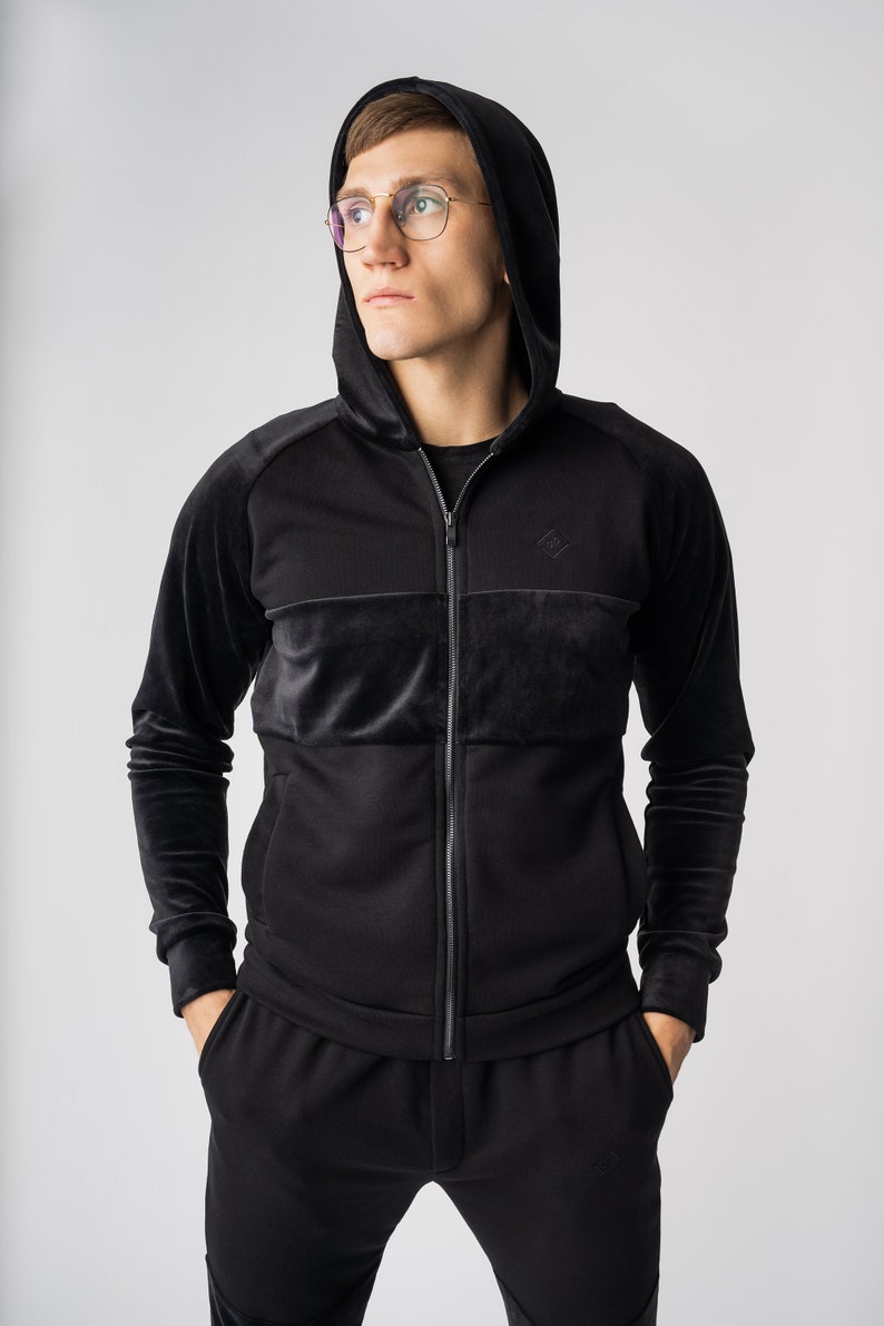 May include: A black zip-up hoodie with a velvet panel and a small diamond logo on the chest. The hoodie has a drawstring hood and long sleeves.