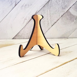 May include: A wooden display stand with a triangular base and three curved arms. The stand is made of light brown wood and has a natural finish.