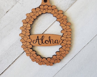 May include: Wooden Christmas ornament shaped like a wreath with the word "Aloha" inscribed on a surfboard inside the wreath.
