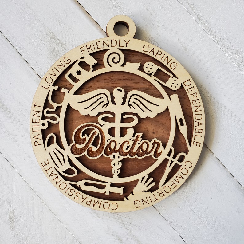 May include: Wooden ornament with a brown background and a medical symbol with wings and a snake. The words "Doctor" are in the center of the ornament. The words "Loving, Friendly, Caring, Dependable, Compassionate, Comforting, Patient" are around the outside of the ornament.