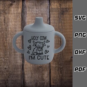 May include: Gray silicone sippy cup with two handles. The cup has a black graphic of a Highland cow with the text "HOLY COW I'M CUTE" and hearts.