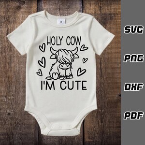 May include: White baby onesie with a black outline of a Highland cow and the text "HOLY COW I'M CUTE" with hearts around the cow.