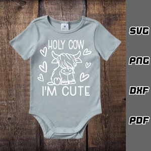 May include: A light blue baby onesie with a white outline of a Highland cow and the text "HOLY COW I'M CUTE" with hearts around the cow.