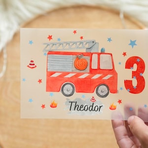 May include: A birthday card featuring a red fire truck illustration with a ladder, hose, and the number 3. The card has the name "Theodor" and is decorated with stars and flames.