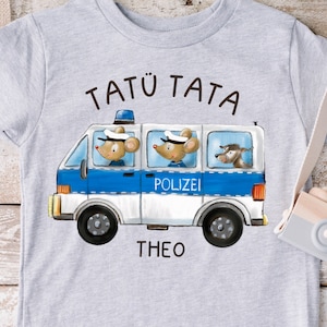 Op de afbeelding: Een grijs T-shirt met een blauwe en witte politiebus met drie muizen erin. De bus heeft het woord "Polizei" aan de zijkant. De tekst "Tatü Tata Theo" staat op het shirt gedrukt.
