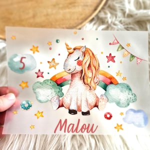 Könnte beinhalten: Ein weißes Einhorn mit einem Regenbogen und Wolken, Sternen und der Zahl 5. Das Einhorn sitzt auf einem Regenbogen mit einer Wolke auf jeder Seite. Der Text "Malou" steht unter dem Einhorn.