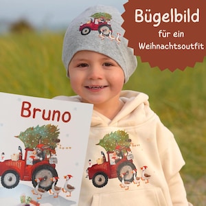 Könnte beinhalten: Ein Kind trägt eine graue Mütze und einen cremefarbenen Kapuzenpullover, beide mit einem roten Traktorgrafik, der einen Weihnachtsbaum und Gänse transportiert. Das Kind hält ein Buch mit dem Namen "Bruno" auf dem Cover. Das Bild enthält auch Text auf Deutsch.