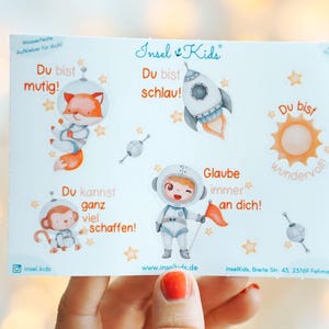 Könnte beinhalten: Ein Bogen mit bunten Aufklebern mit Cartoon-Astronauten, einem Fuchs, einem Affen, einer Rakete und einer Sonne. Der Text enthält Sätze wie "Du bist mutig", "Du bist schlau" und "Glaube an dich!" Die Aufkleber sind für Kinder.