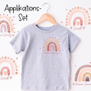 Puede incluir: Un conjunto de cuatro aplicaciones termoadhesivas con arcoíris de acuarela con diferentes textos en alemán. Los arcoíris son en tonos de rosa, naranja y marrón. Los textos incluyen "Kleiner Schatz", "Geliebt" y "Kleiner Sonnenschein".