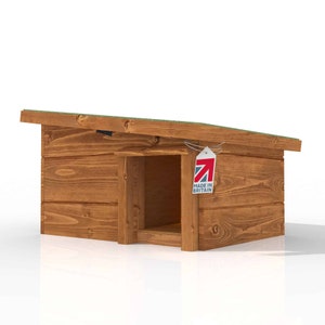 May include: A small wooden dog house with a sloping roof and an open entrance. The dog house is constructed from brown wood and features a green roof. A tag reading "MADE IN BRITAIN" is attached.