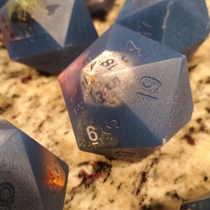 May include: A set of blue, multi-sided dice with white numbers. The dice are made of a textured material and have a speckled appearance. The numbers on the dice are 1, 2, 3, 4, 5, 6, 7, 8, 9, 10, 11, and 12.