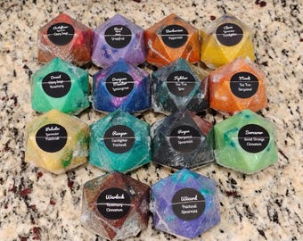 May include: A collection of fourteen multi-faceted, polyhedral-shaped soaps wrapped in clear plastic. Each soap features a circular black label with white text identifying a character class and scent, including Artificer, Bard, Barbarian, Cleric, Druid, Dungeon Master, Fighter, Monk, Paladin, Ranger, Rogue, Sorcerer, Warlock, and Wizard.