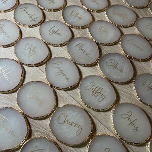 May include: A set of 20 white round coasters with gold trim and gold lettering. Each coaster has a different name written on it.
