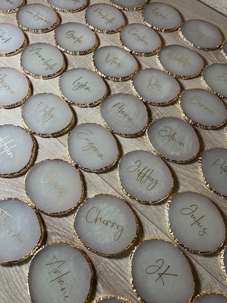 May include: A set of 20 white round coasters with gold trim and gold lettering. Each coaster has a different name written on it.