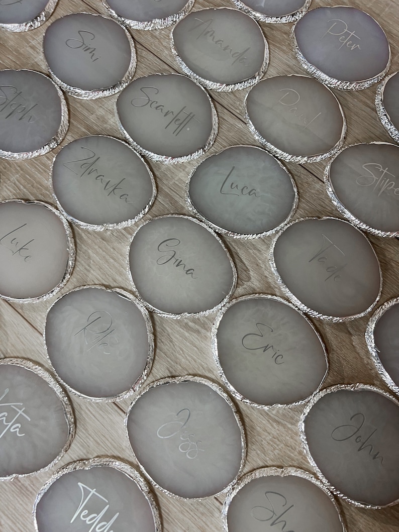 May include: A set of 18 gray agate coasters with silver trim. Each coaster has a name written on it in white script. The names include: Peter, Amanda, Stipe, Simi, Scarletl, Luca, Tade, Joph, Zdravka, Gina, Cric, John, Luke, ch, Sh, Tedd.