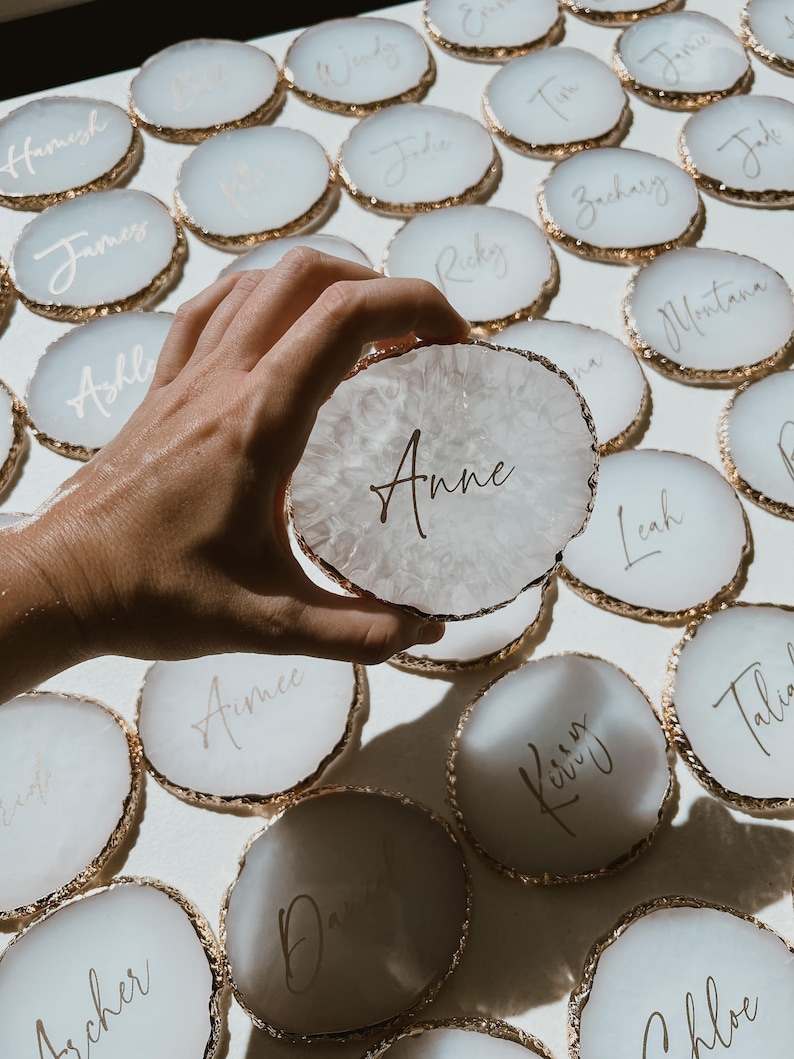 May include: White agate coasters with gold trim and names written in gold calligraphy. The names include Anne, Aimee, Archer, David, Chloe,  and more.